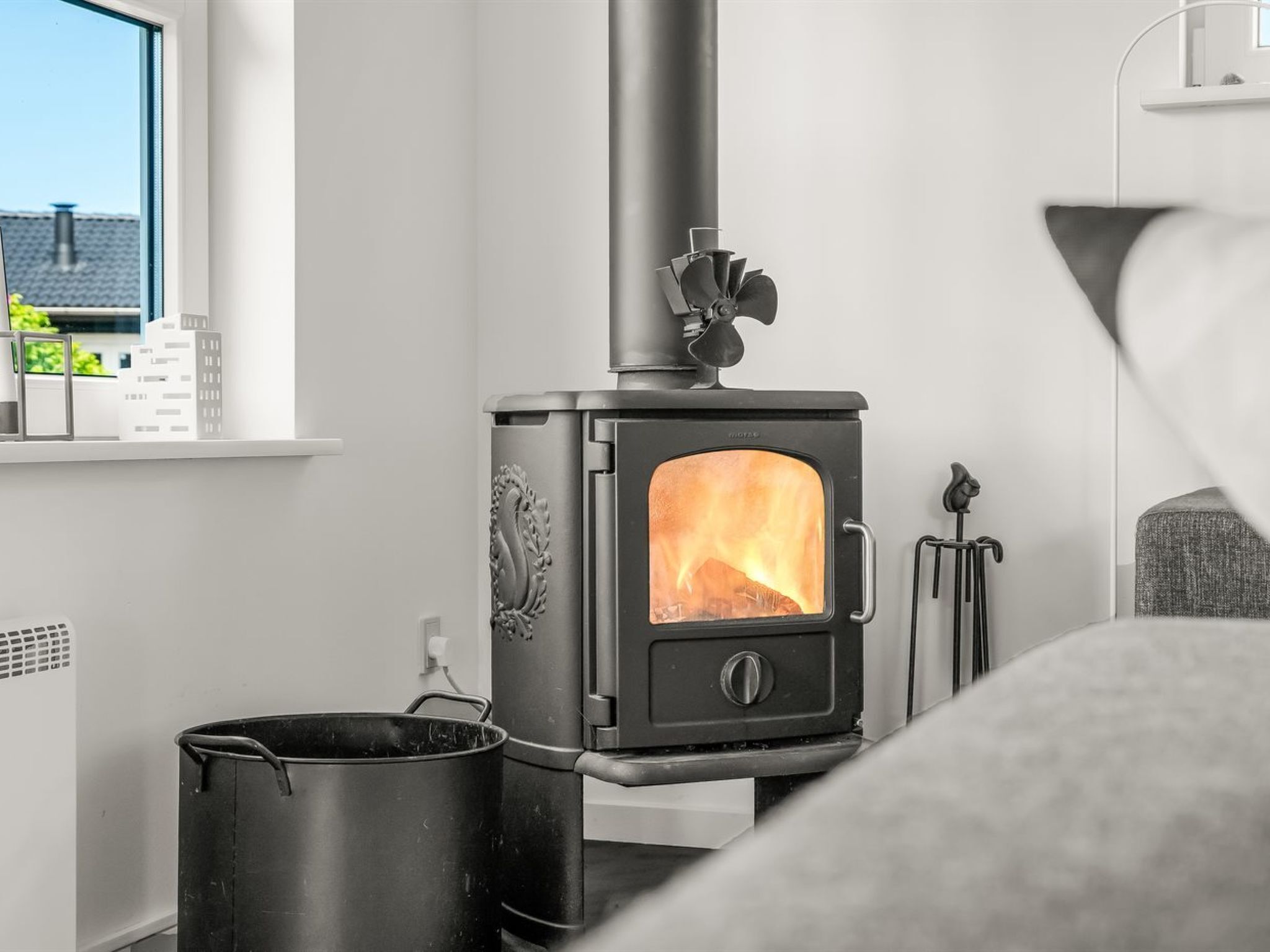 Een moderne woonkamer met een zwart houtkachel, een raam met uitzicht op gebouwen en een radiator.
