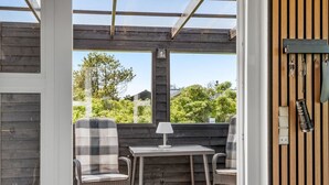Ein überdachter Patio-Bereich mit Tisch und zwei Stühlen, einer Lampe und Blick auf Grünflächen.