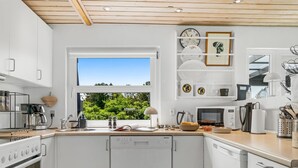 Eine moderne Küche mit weißen Schränken, einem eingebauten Backofen, einem Geschirrspüler, einem Fenster mit Blick auf Grünflächen und verschiedenen Küchengeräten.