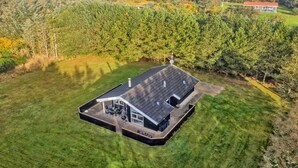 Ett modernt hus med en stor terrass och utsikt över ett skogsområde.