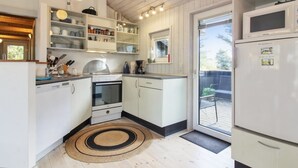 Ett kompakt kök med vita skåp, en inbyggd ugn och en mikrovågsugn. Det finns en liten köksö med en diskho och en rund, vävd matta på golvet.