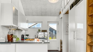 Une cuisine moderne avec des meubles blancs, un îlot central et une vue sur l’extérieur.