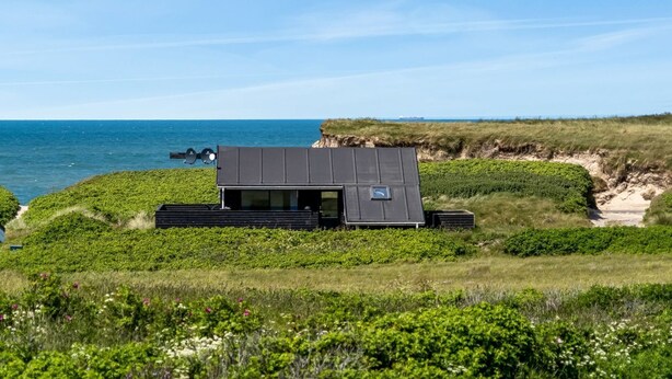 Une maison moderne, dotée d’un toit plat, située sur une colline verdoyante qui offre une vue sur la mer.