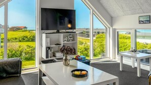 Un salon moderne doté d’un grand téléviseur, de meubles blancs et offrant une vue sur la verdure environnante.