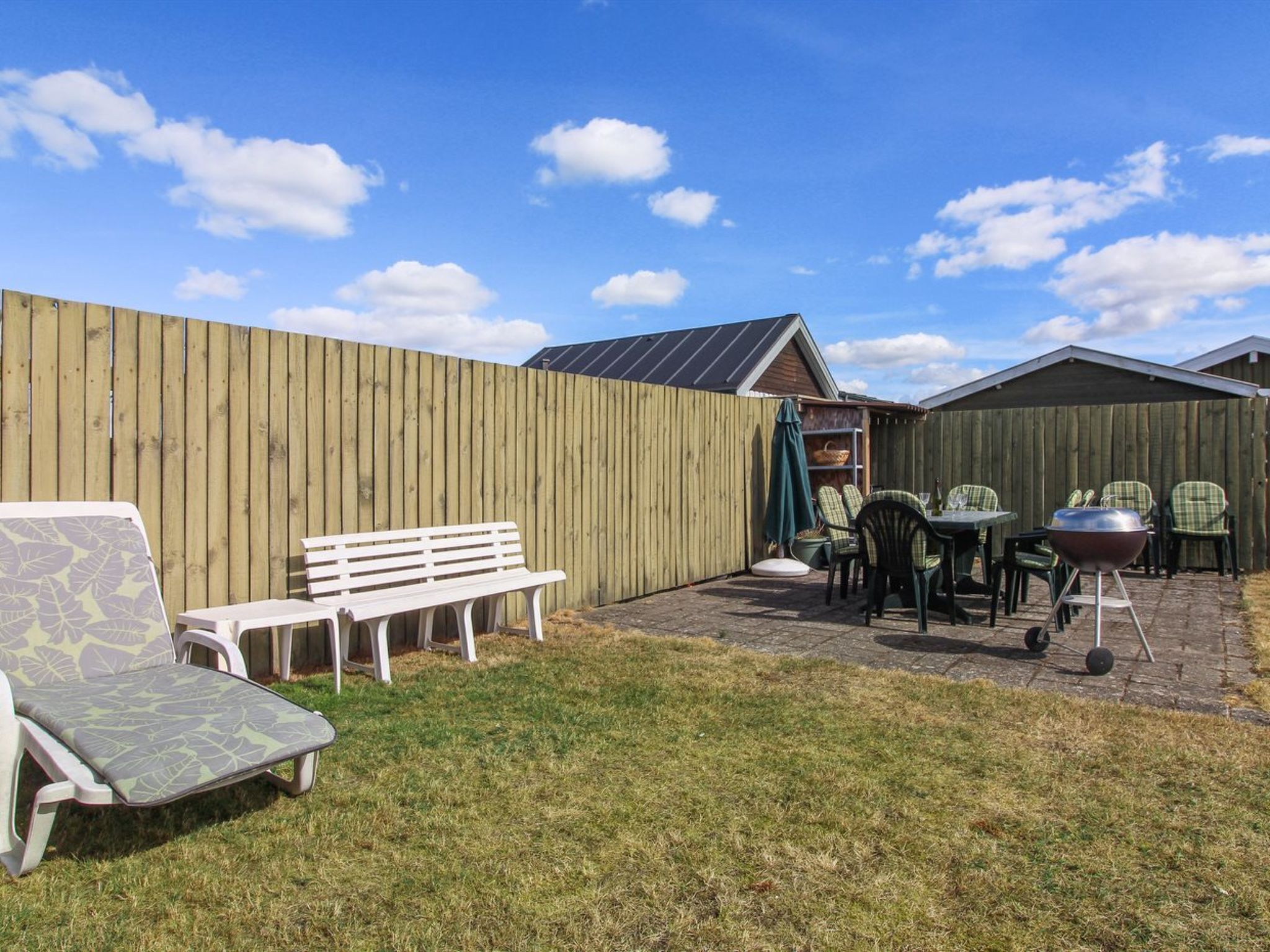 Un jardin avec une clôture en bois, un banc blanc, une table avec des chaises et un barbecue.