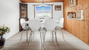 Un espace repas doté d’un plafond en bois, de chaises blanches, d’une table centrale et offrant une vue sur le paysage urbain à travers une grande fenêtre.