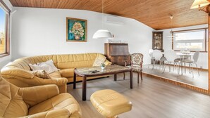 Un salon moderne avec un plafond en bois, un canapé, une table basse et un coin repas comprenant des chaises et une table.