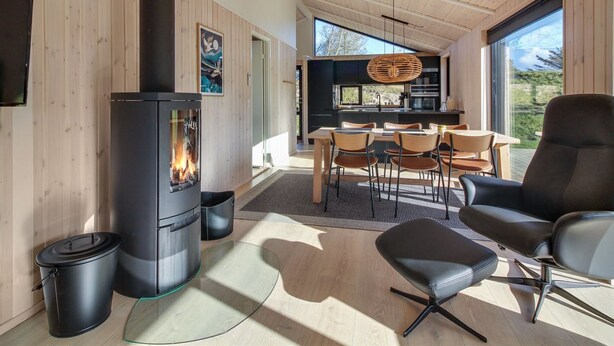A modern interior with a wood-paneled room, a fireplace, a dining area with chairs, and a kitchen visible through an open door.