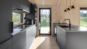 A modern kitchen with dark cabinetry, a black countertop, and a large window providing a view of the outdoors.