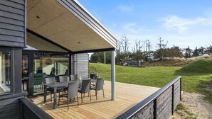 A covered outdoor area with a table and chairs, a grill, and a view of a grassy landscape.