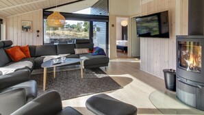 A modern living room with a sofa, coffee table, and fireplace. There is a TV mounted on the wall and a window providing a view of the outdoors.