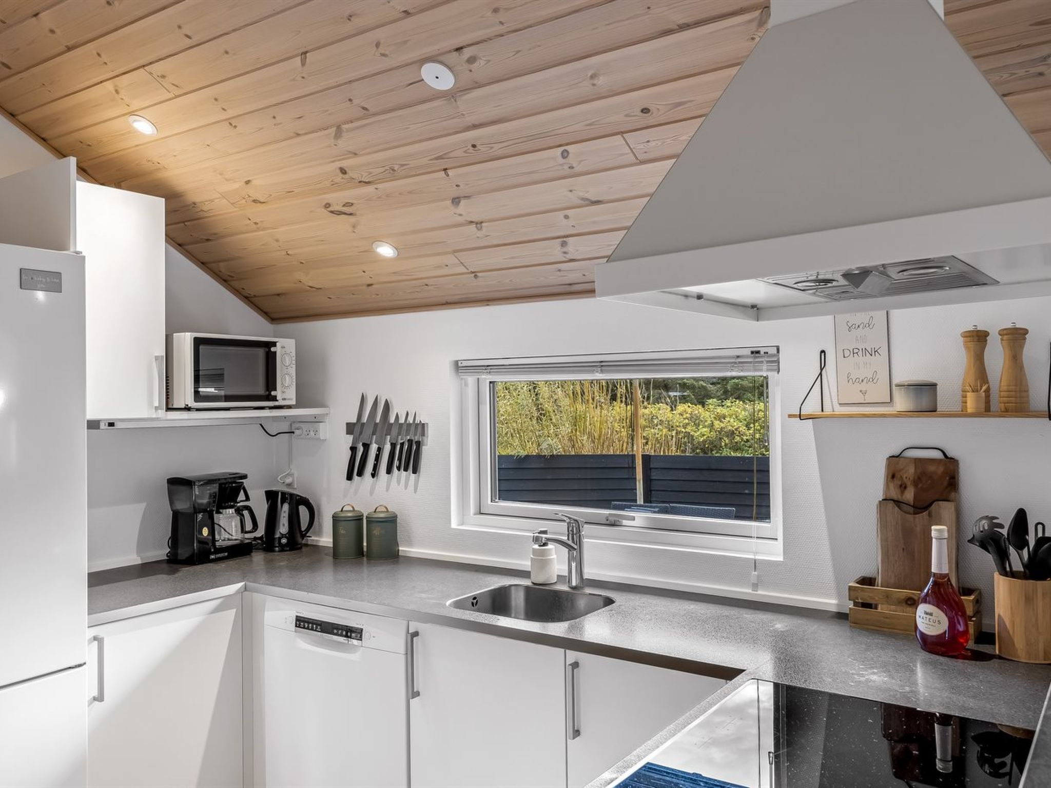Una cocina moderna con techo de madera, ventana con vistas y diversos electrodomésticos.