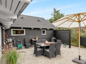 Une terrasse avec une table et des chaises, un enrouleur de tuyau d’arrosage et un grand parasol.