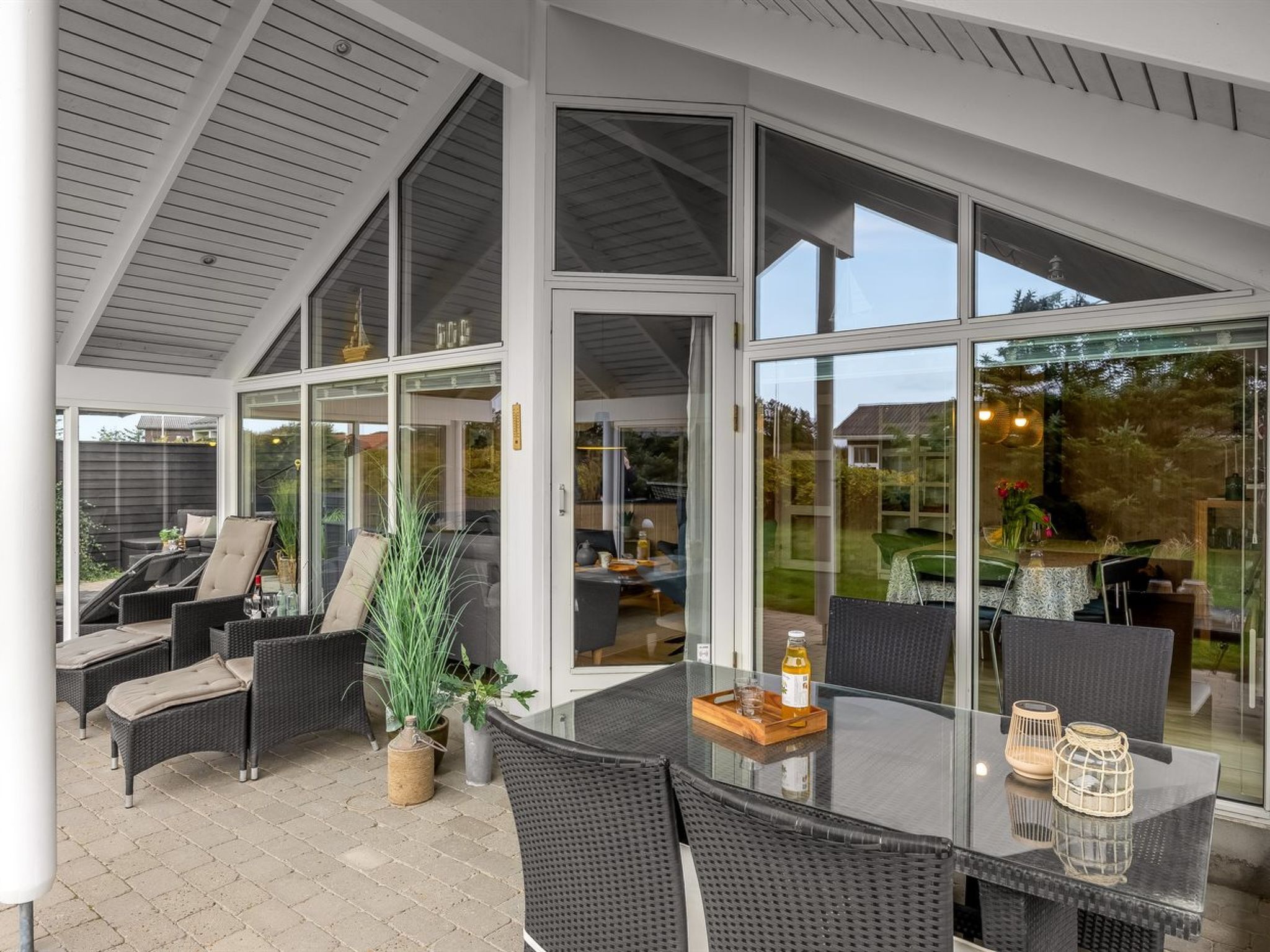Een overdekt terras met rieten meubels en een glazen tafel, met uitzicht op het interieur.