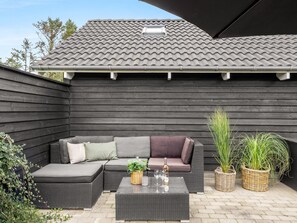 A patio area with a dark-colored sofa, a small table, and two wicker baskets with plants.