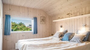 A bedroom with a wooden ceiling and walls, a large bed with multiple pillows, a window with curtains, and a small bedside table with a lamp. - "Federica" - 500m from the sea by Interhome (Løkken)