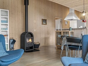 Un salon moderne avec un mur lambrissé, une cheminée noire et un coin repas comprenant une table et des chaises.
