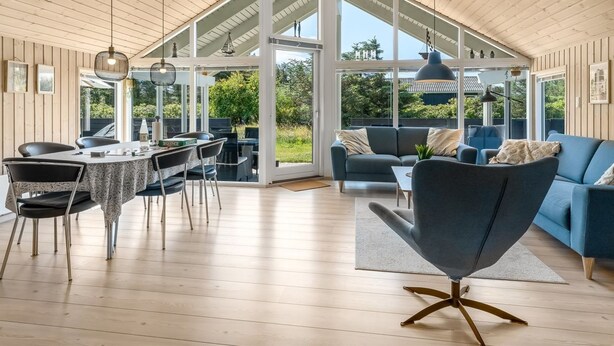 A spacious room with a high ceiling, a dining area with a table and chairs, a blue sofa, and a large window offering a view of the outdoors. - "Federica" - 500m from the sea by Interhome (Løkken)