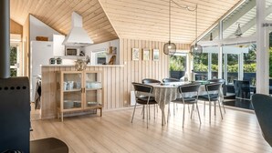 A modern kitchen with wooden paneling, a dining area with a table and chairs, and a large window overlooking greenery. - "Federica" - 500m from the sea by Interhome (Løkken)