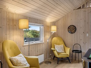 A room with wooden walls, a window, two lamps, a dartboard, and two armchairs.