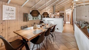A spacious dining area with a wooden table and chairs, a kitchen in the background, and a large window providing natural light.