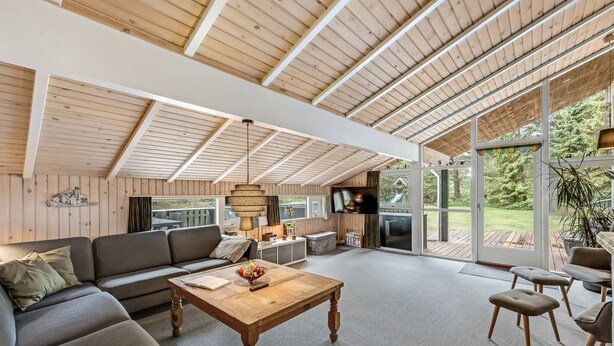 A spacious living area with a wooden ceiling, a large sofa, a coffee table, and a television.