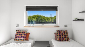 A bedroom with two beds, a window with a view of trees, and a small table.