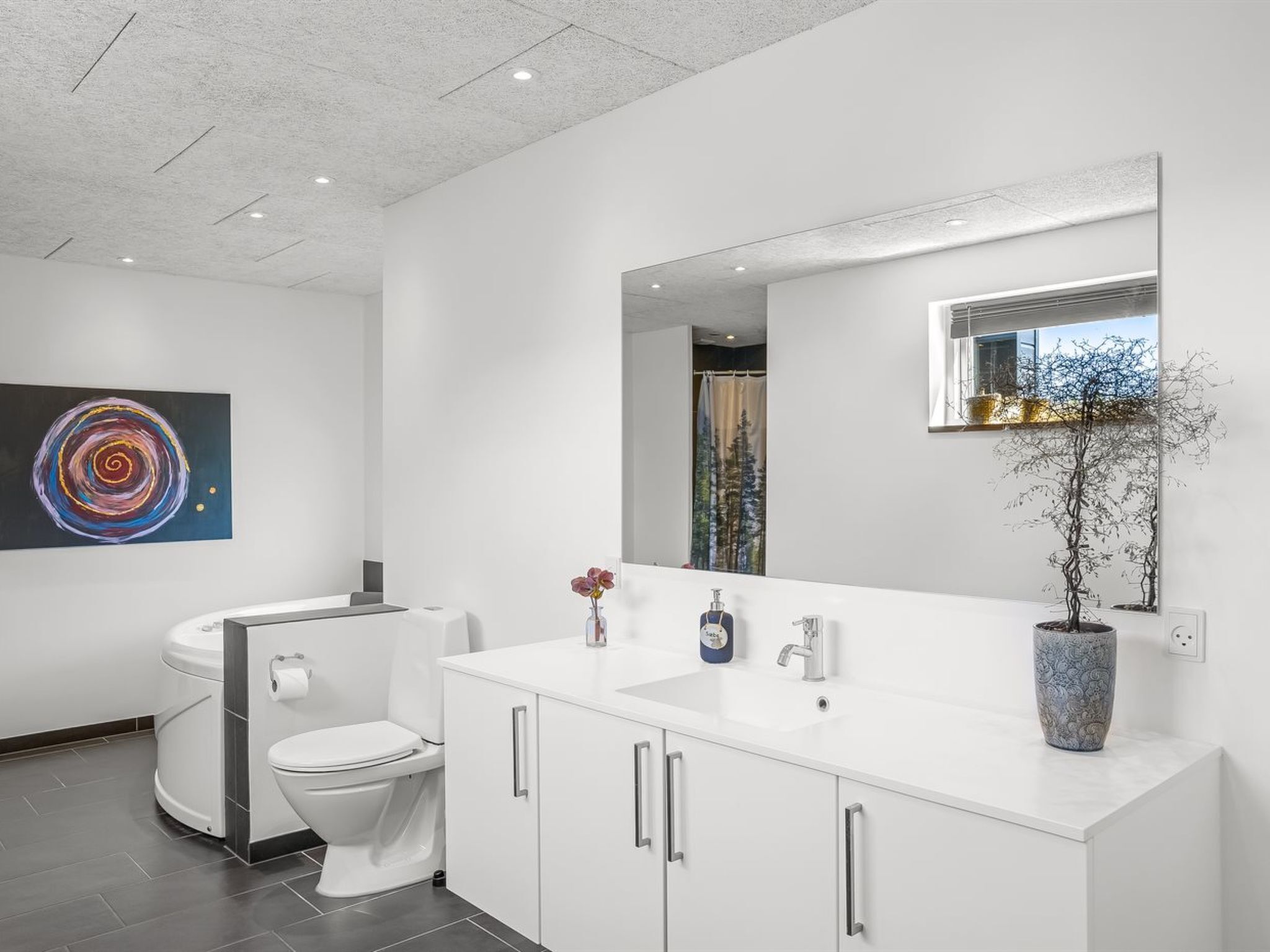A modern bathroom with a white vanity, a large mirror, and a painting on the wall.