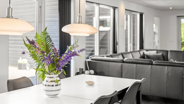 A modern living room with a dining area, large windows, and a grey sofa.