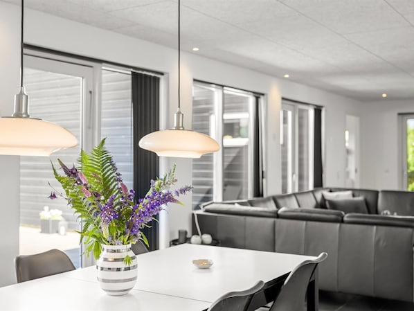 A modern living room with a dining area, large windows, and a grey sofa.