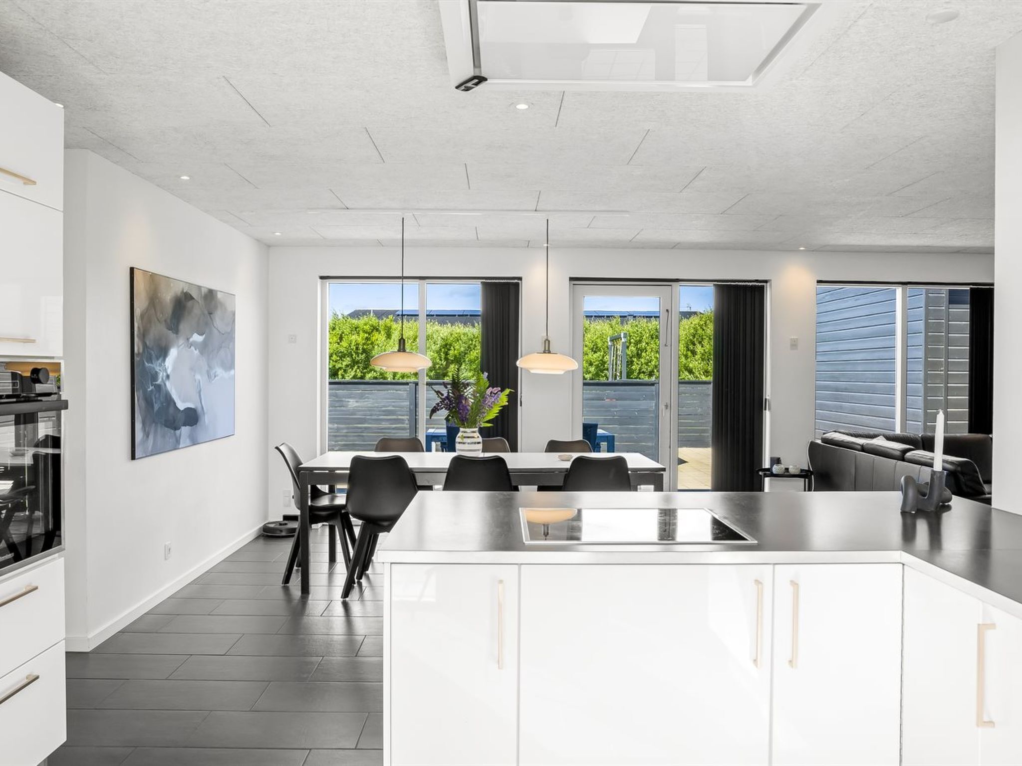 A modern kitchen with a central island, dining area with chairs, and large windows offering a view of greenery.