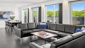 A modern living room with a sectional sofa, a dining area, and large windows.