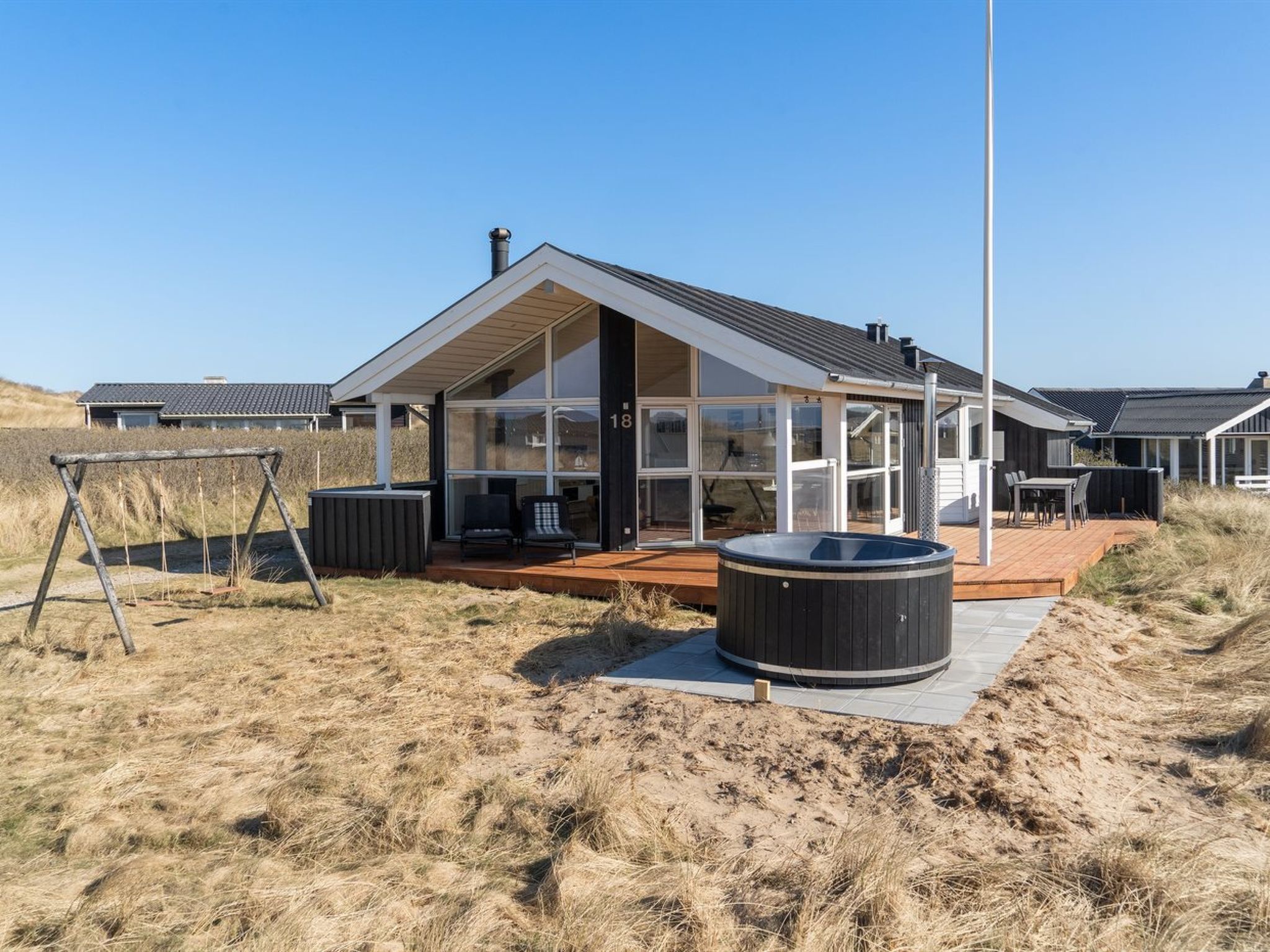 A modern house with large glass windows, a wooden deck, and a hot tub.