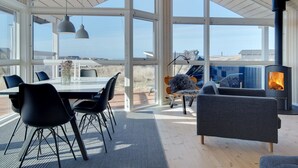 A modern interior with a large glass wall, a dining area, and a wood-burning stove.
