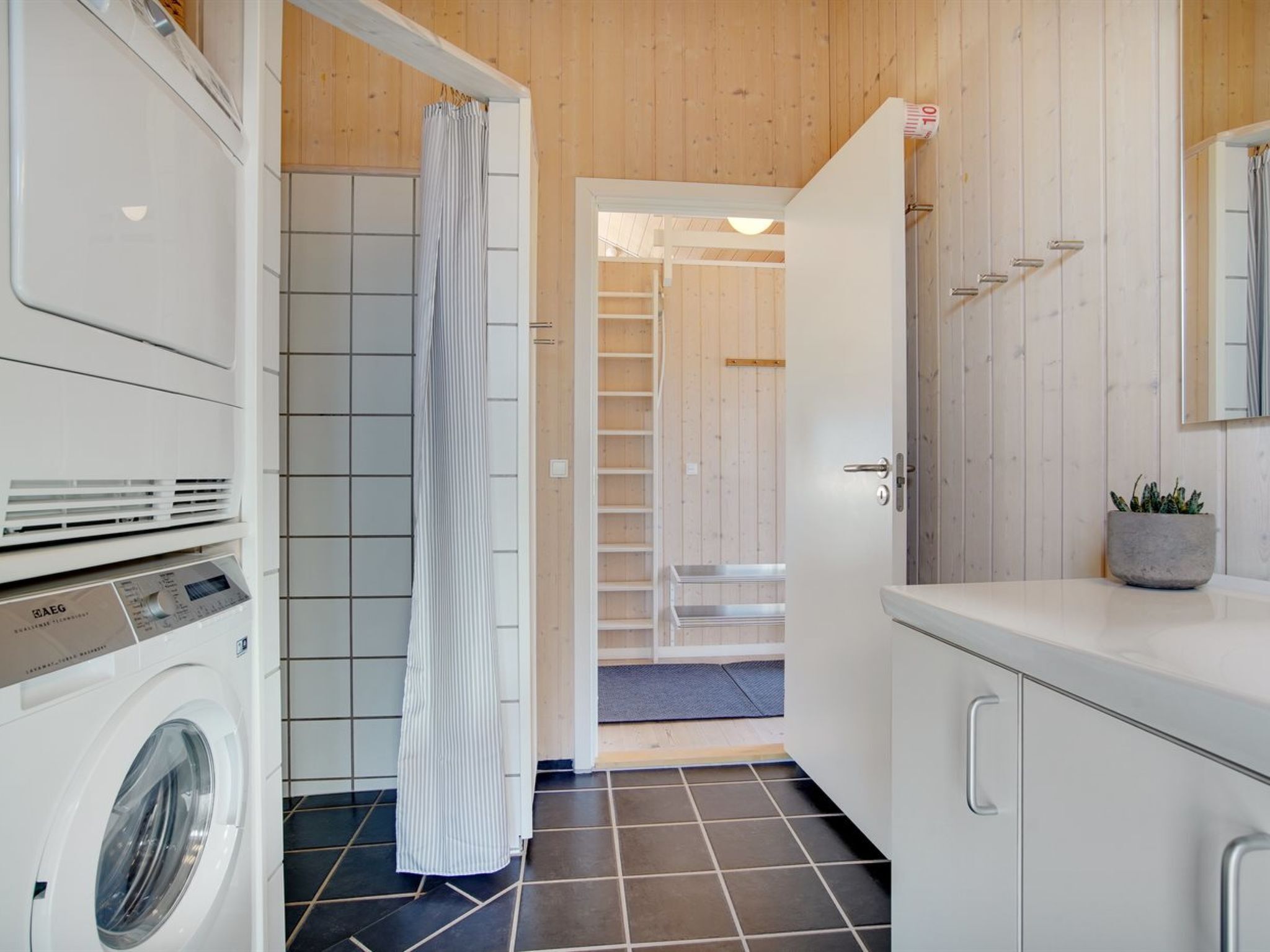 A modern laundry room with a washing machine, dryer, and a shower area with a striped curtain.