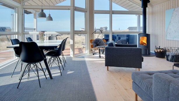 A spacious living area with a large open-plan layout, featuring a dining table, chairs, a sofa, and a wood-burning stove.