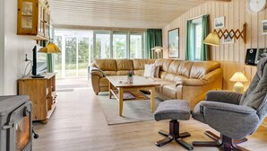 A cozy living room with a leather sofa, a wooden coffee table, and a grey armchair. There is a wooden cabinet with a television and a fireplace.