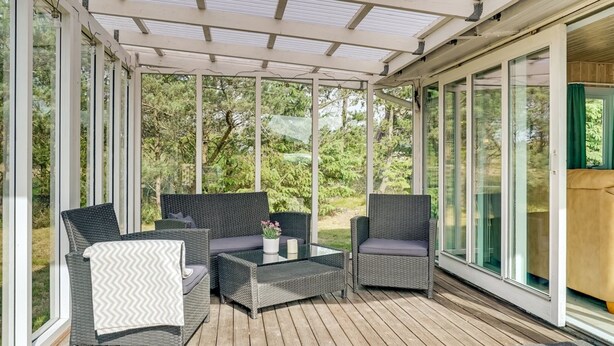 A covered outdoor seating area with wicker furniture and a glass enclosure.