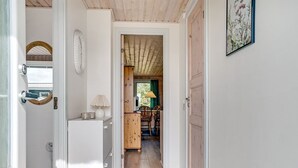 A hallway leading to a dining area with a wooden ceiling, a table with chairs, and a lamp.