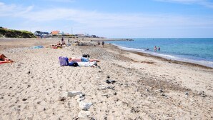 Ein Strand mit badenden und sonnenden Personen sowie Gebäuden im Hintergrund.