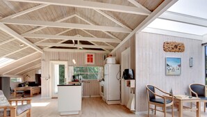 Ein geräumiger Loft mit hoher Decke, Holzbalken, einer Küche mit Kühlschrank und einem Essbereich mit Stühlen.