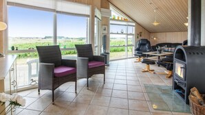 A spacious room with large windows, a fireplace, wicker furniture, and a view of the countryside.