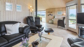 A spacious living area with a wooden ceiling, leather sofas, a coffee table, and a television.
