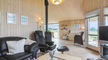 Un vaste espace de vie doté d’un plafond en bois, de canapés en cuir, d’une table basse et d’un téléviseur.