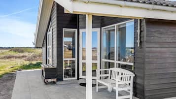 Une maison moderne dotée d’un porche abrité, de grandes fenêtres et d’un banc.