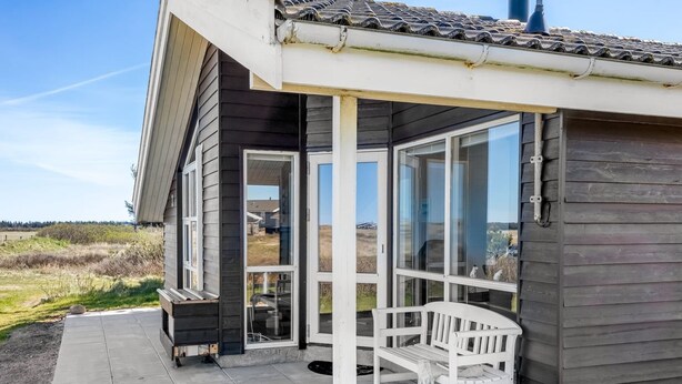 A modern house with a covered porch, large windows, and a bench.