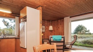 Eine kompakte Küche mit Holzausstattung, einem weißen Kühlschrank, einem Esstisch mit Stühlen und Blick ins Freie durch große Fenster.