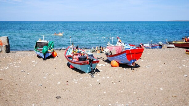 Ein Strand mit mehreren vertäuten Booten, blauem Himmel und ruhiger See.