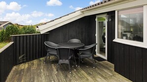 A covered patio with a table and chairs, a sliding glass door, and a view of the surrounding area.