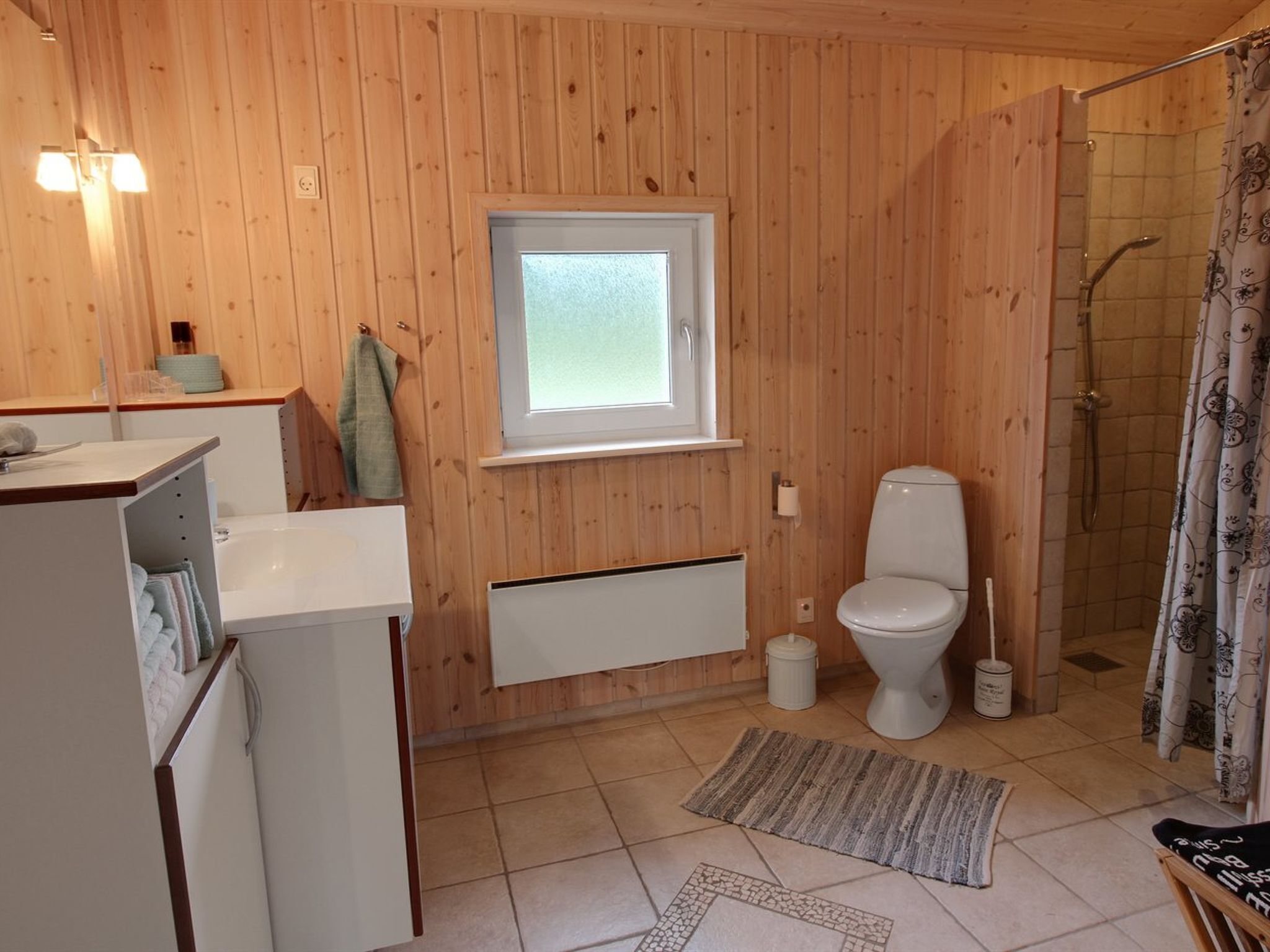 Ein Badezimmer mit Holzwandverkleidung, einem Fenster, Toilette, Dusche und einer kleinen Spüle.